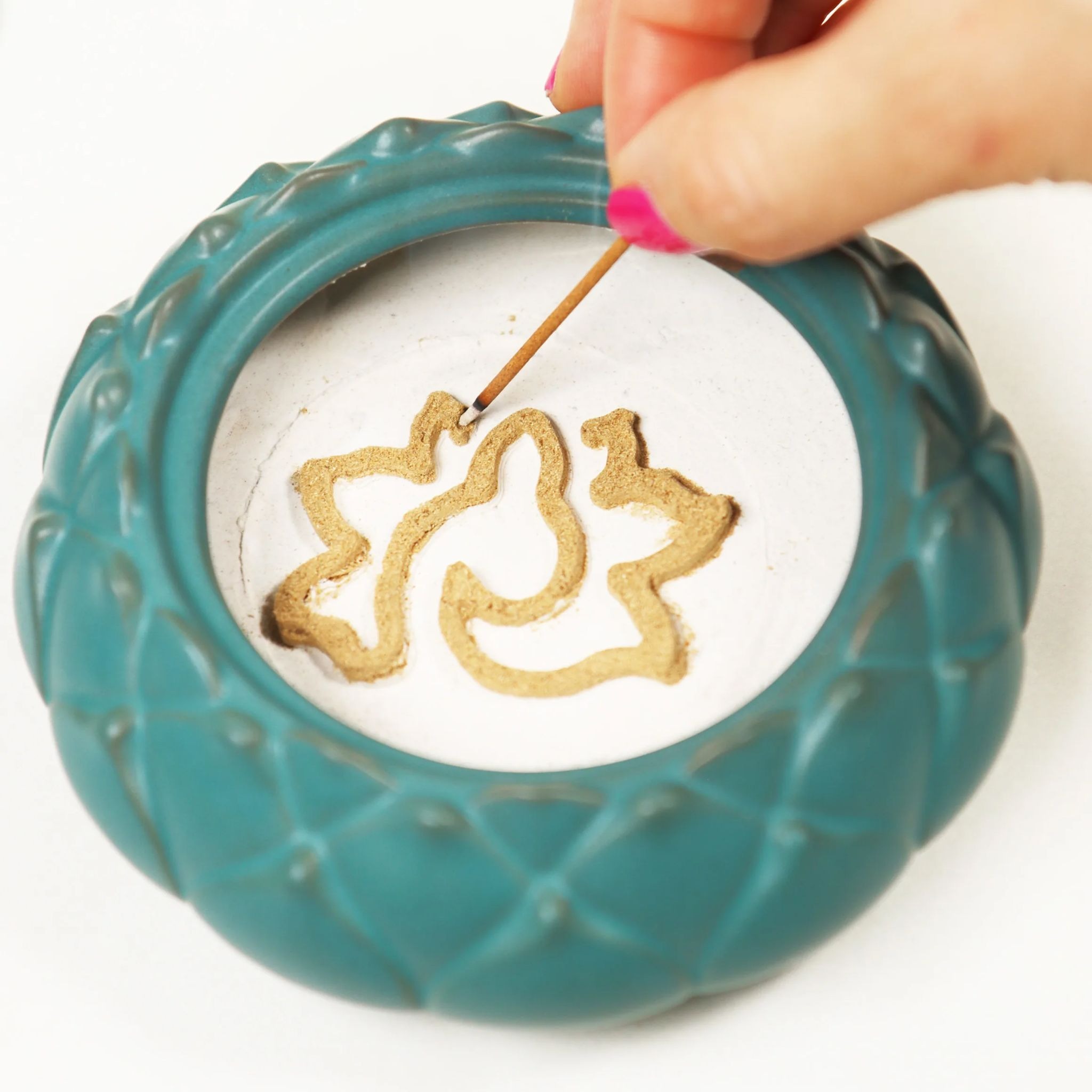 Hand lighting intricate incense powder pattern inside a teal ceramic incense sealing burner.