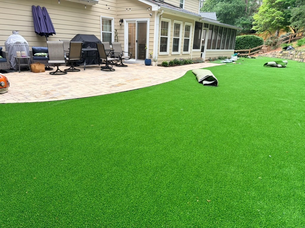 Large residential backyard featuring premium artificial grass installation beside a patio and outdoor seating area.