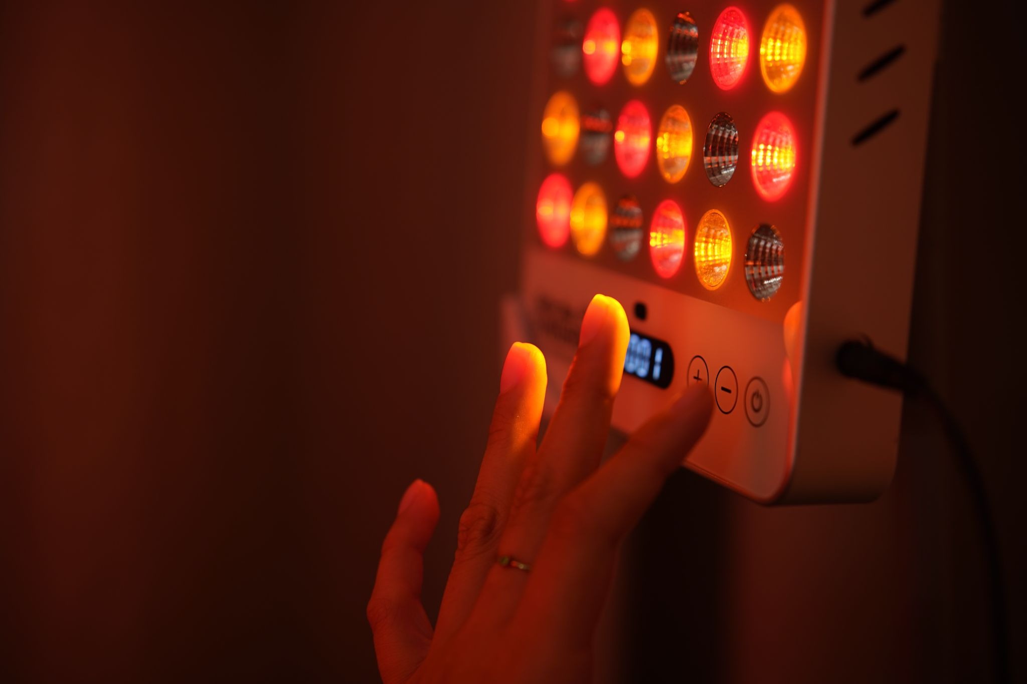 Hand adjusting glowing Mitolux red light therapy lamp controls in dark room.