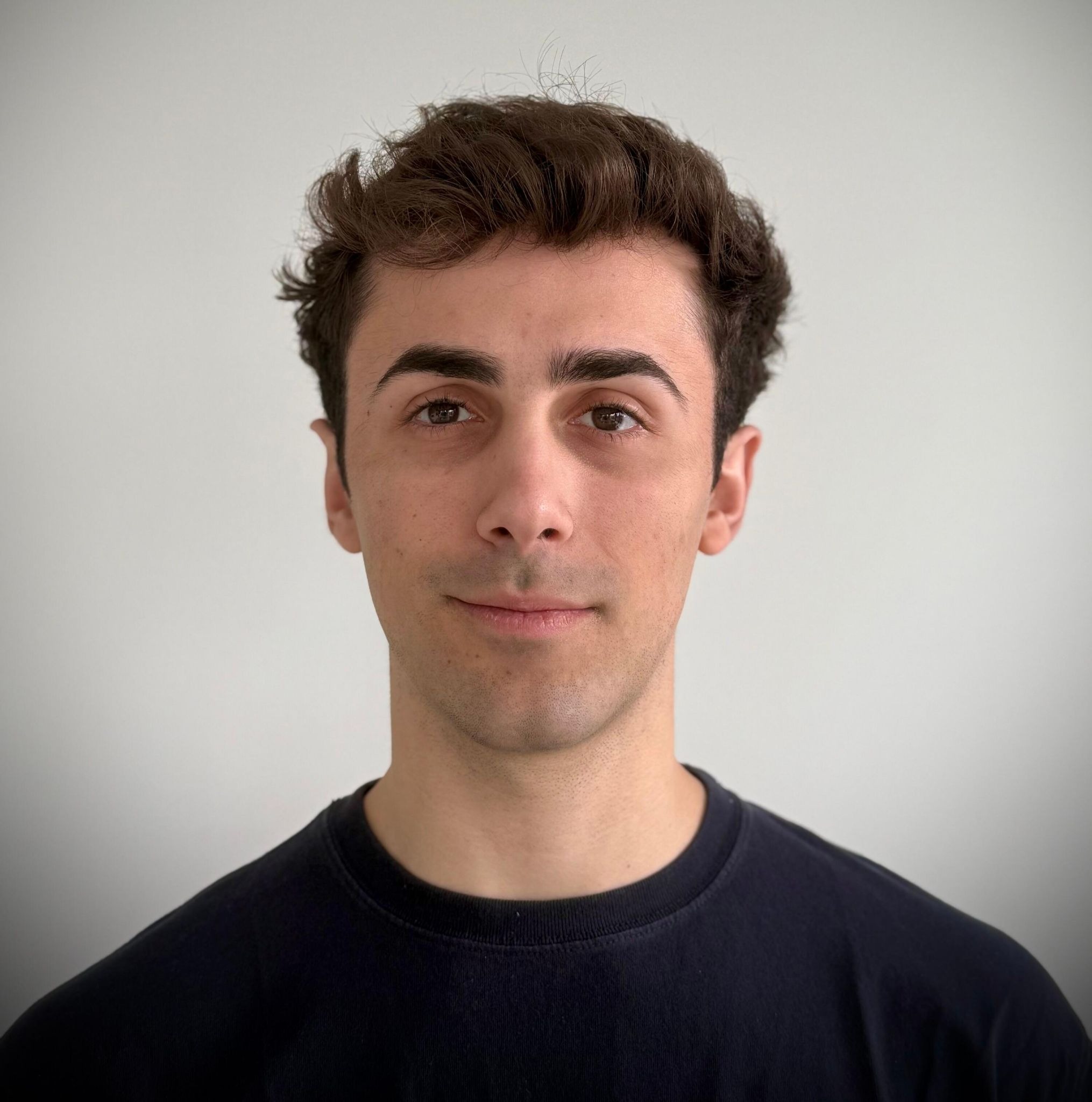 Young man with dark hair wearing black shirt against plain white background.