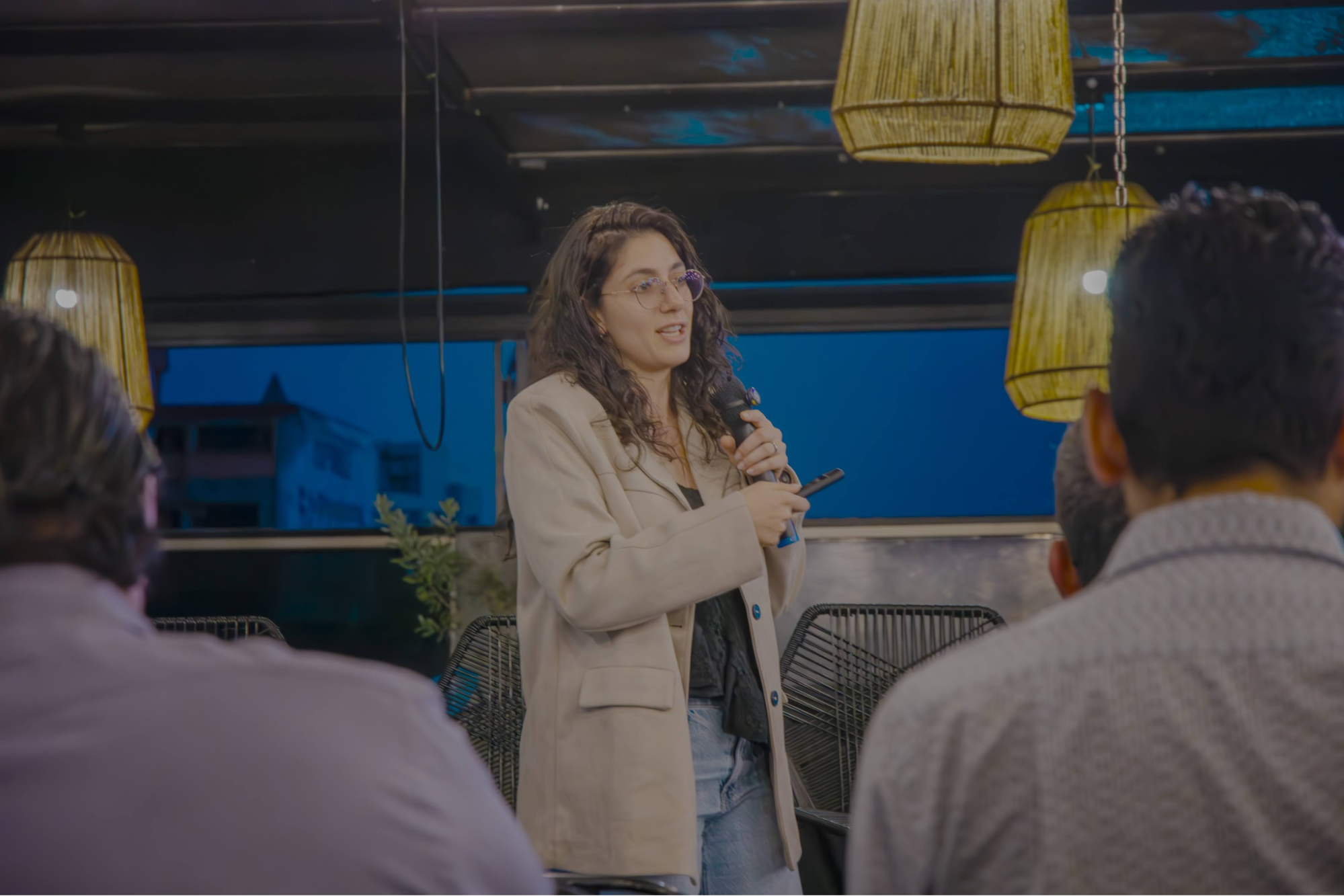 Woman speaking into a microphone during a presentation to a small audience indoors.