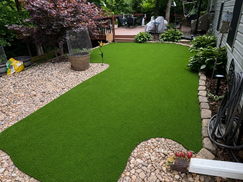 Backyard artificial turf installation with stone landscaping and a wooden deck in a residential outdoor space.