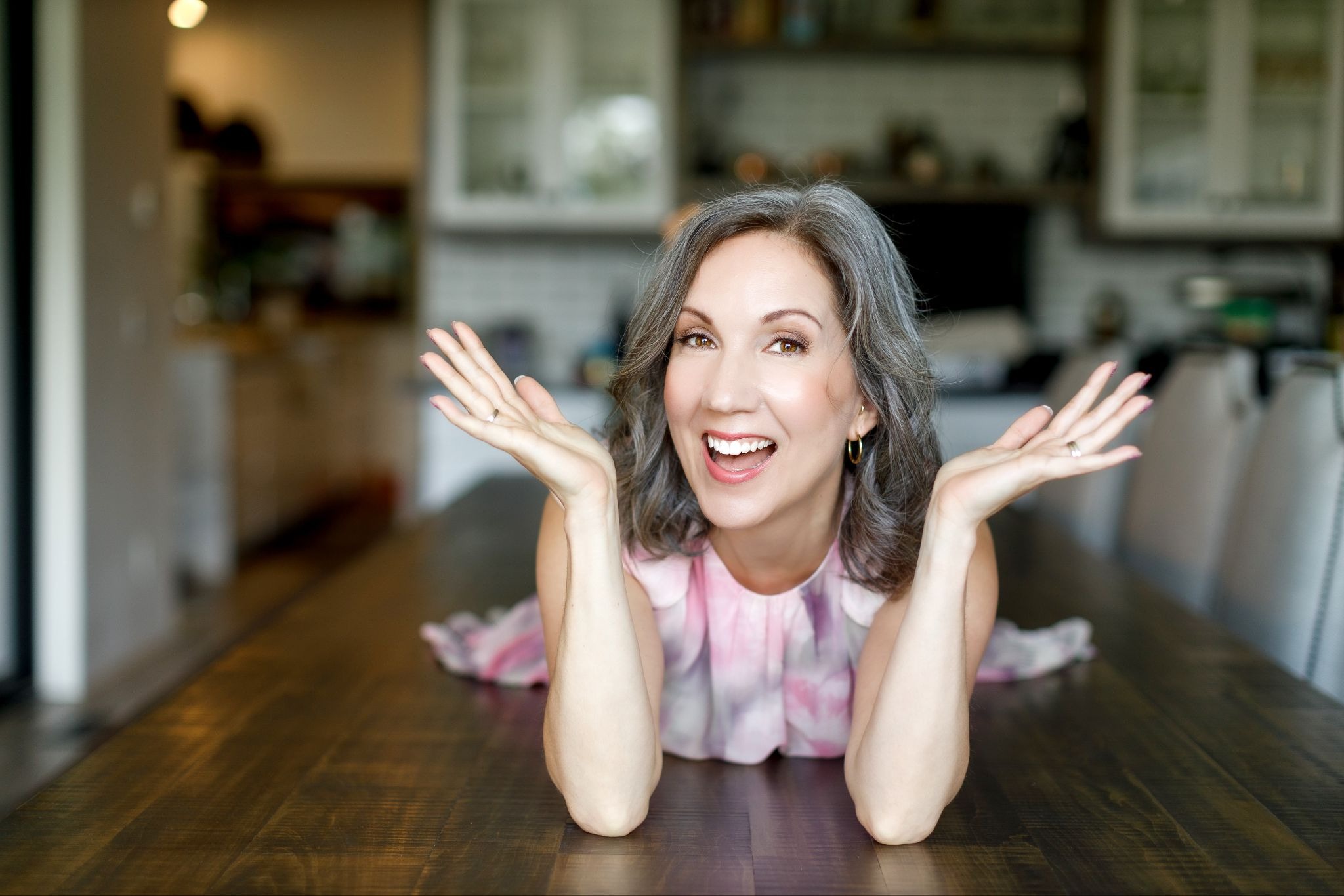 Woman dentist smiling with hands raised while leaning on wooden table at home.