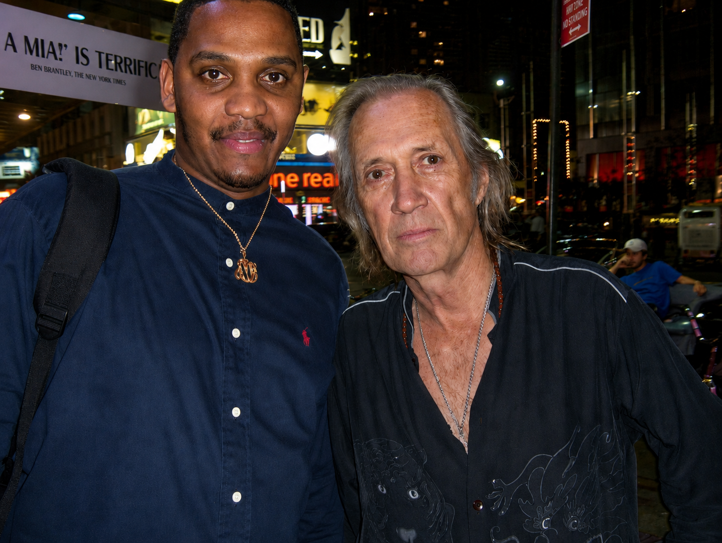 Man posing beside older musician outside a theater at night.