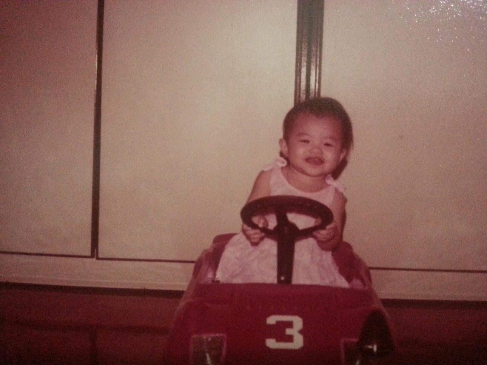 A young girl in a red toy car, capturing the essence of fun and adventure in her playful expression.