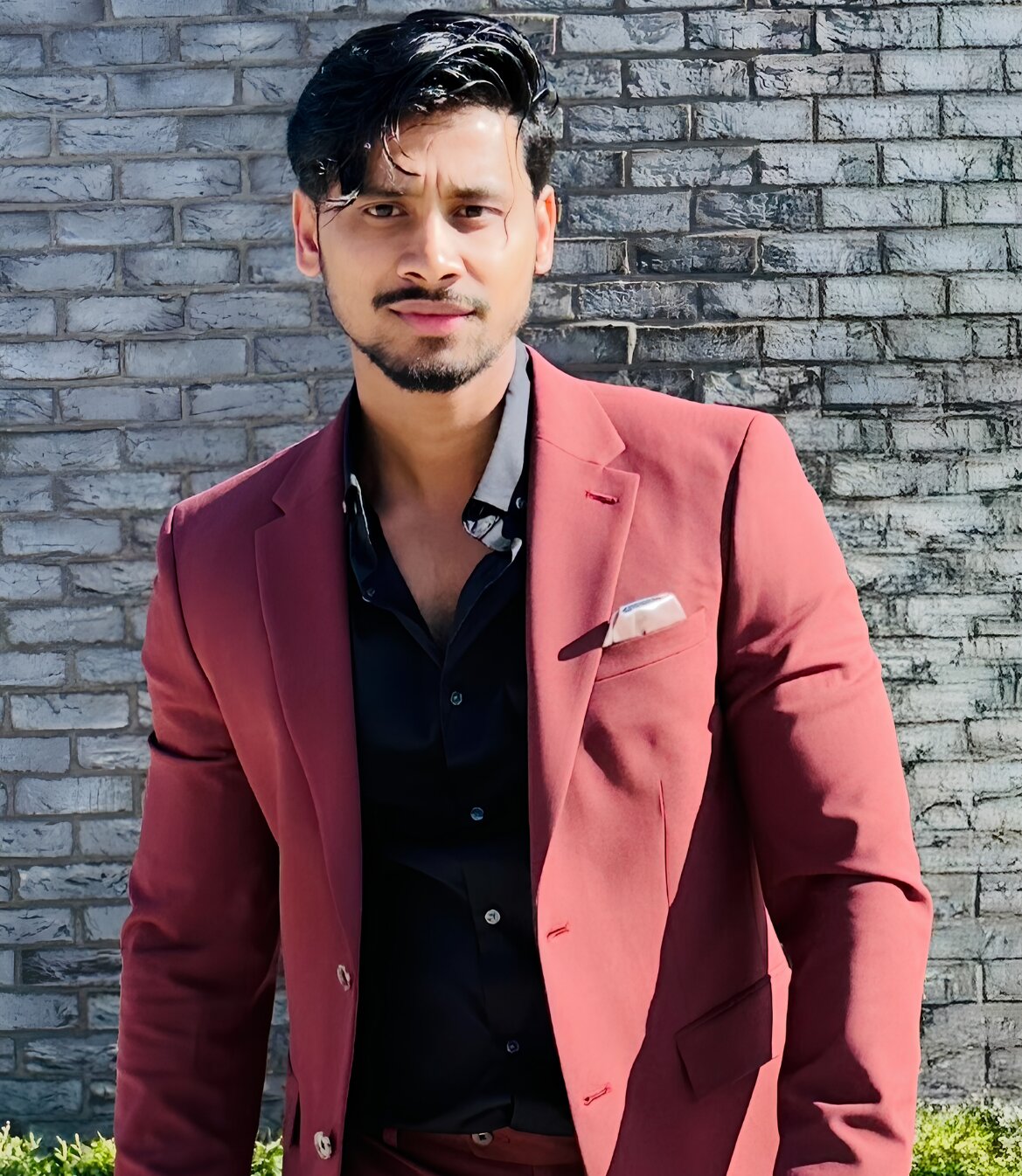 A man in a red suit stands confidently in front of a textured brick wall, embodying a professional and innovative spirit.