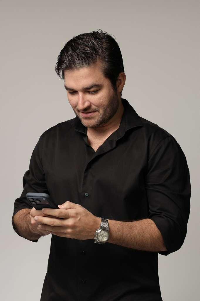 Luxury watch market specialist wearing a black shirt, looking at a smartphone while wearing a wristwatch.