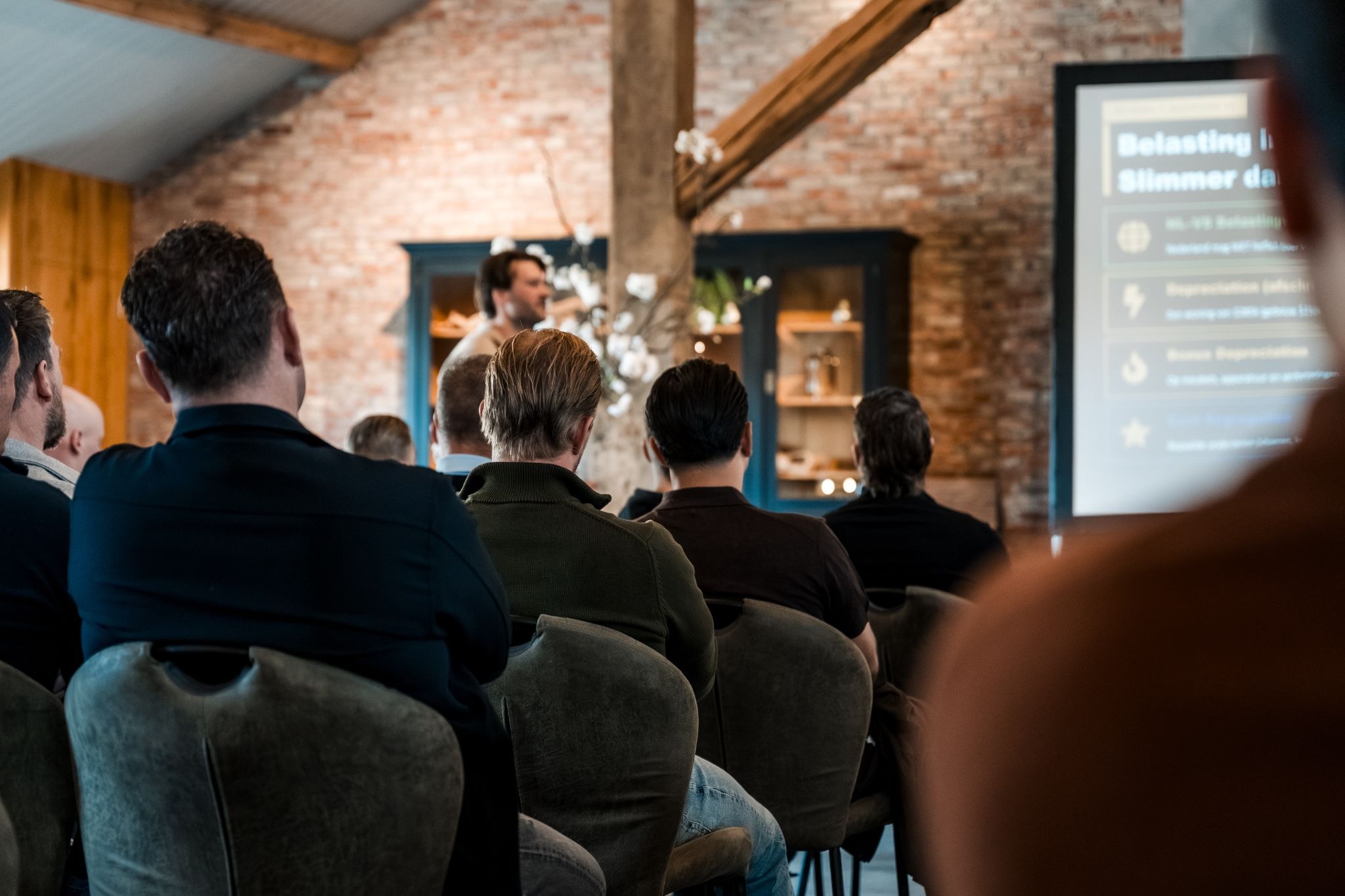 Audience attends Subject2Success real estate presentation in a rustic venue with speaker addressing investors.