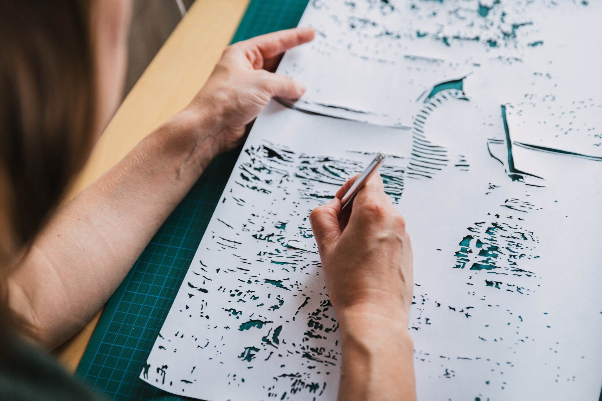 Artist cutting intricate paper artwork with a scalpel on a worktable.