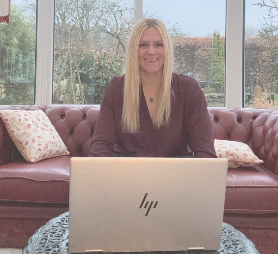 Sarah Darracott Hawkins smiling behind a laptop in a bright conservatory, representing We Love PMO's business systems consultancy.