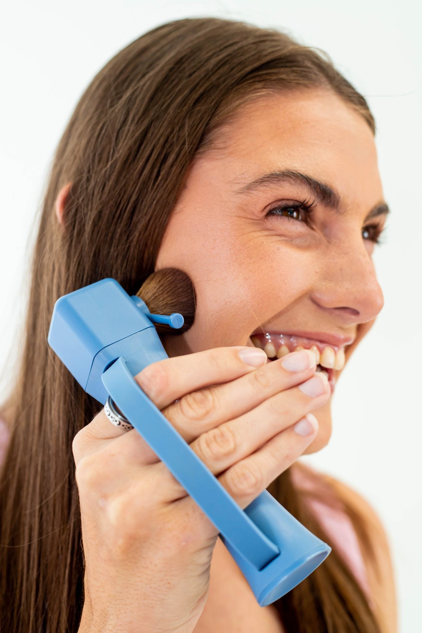 Smiling woman applies makeup with ergonomic Flexxi Beauty brush designed for easier grip and control.