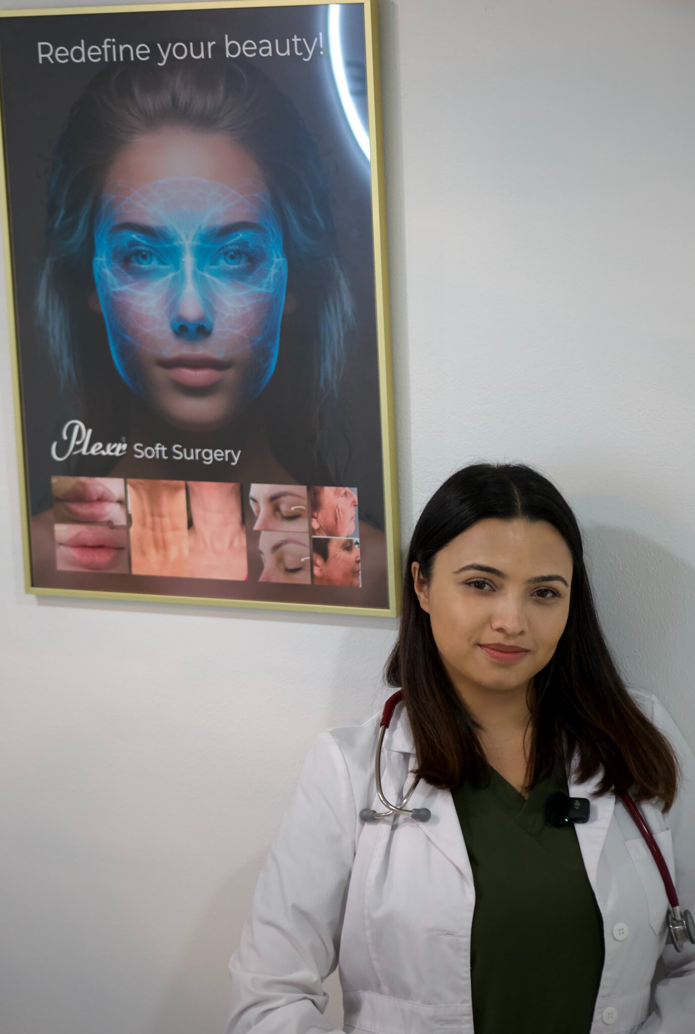 ARBOUR founder and clinician standing beside aesthetic treatment poster in clinic office.