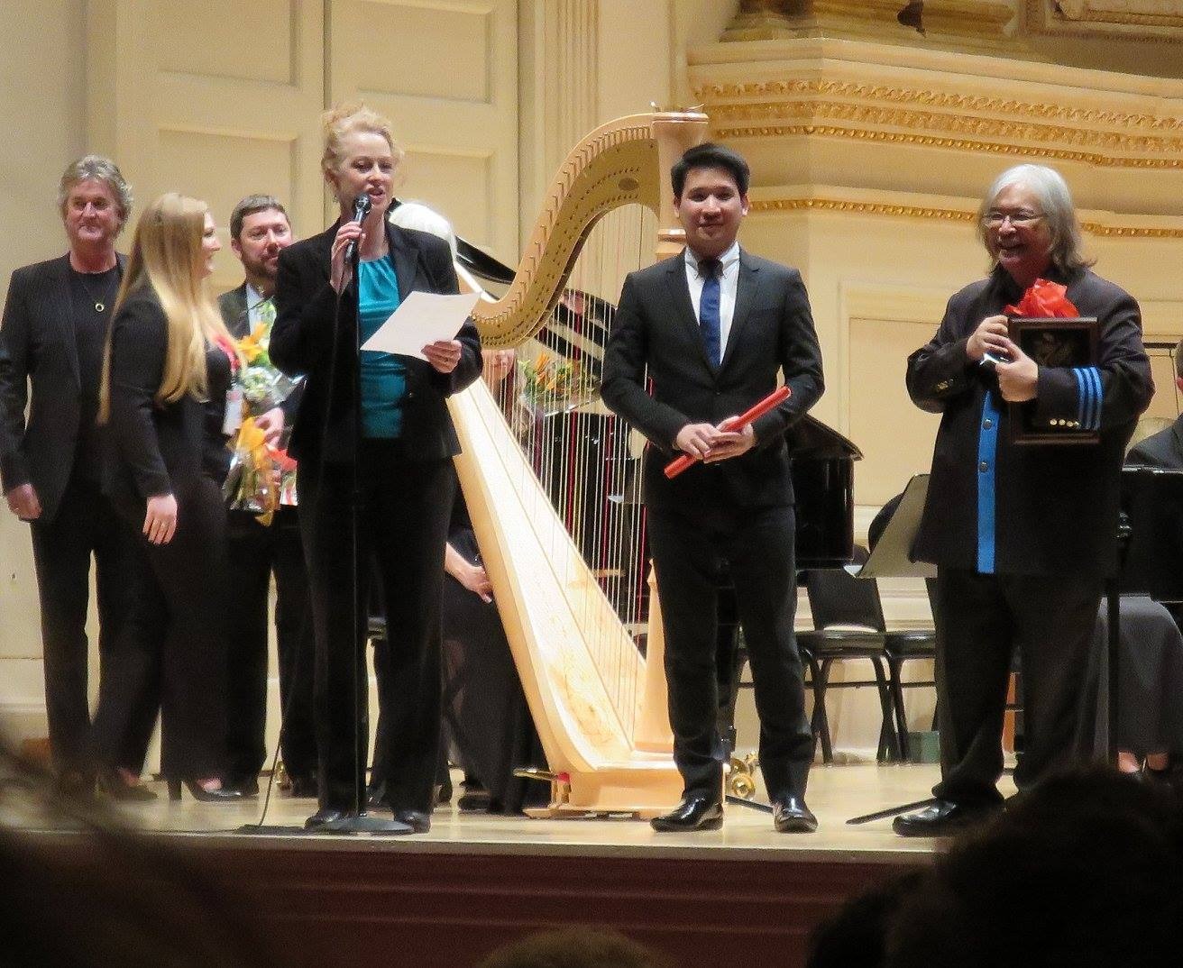 Somtow Sucharitkul and Trisdee na Patalung accept an award onstage at Carnegie Hall with orchestra members.