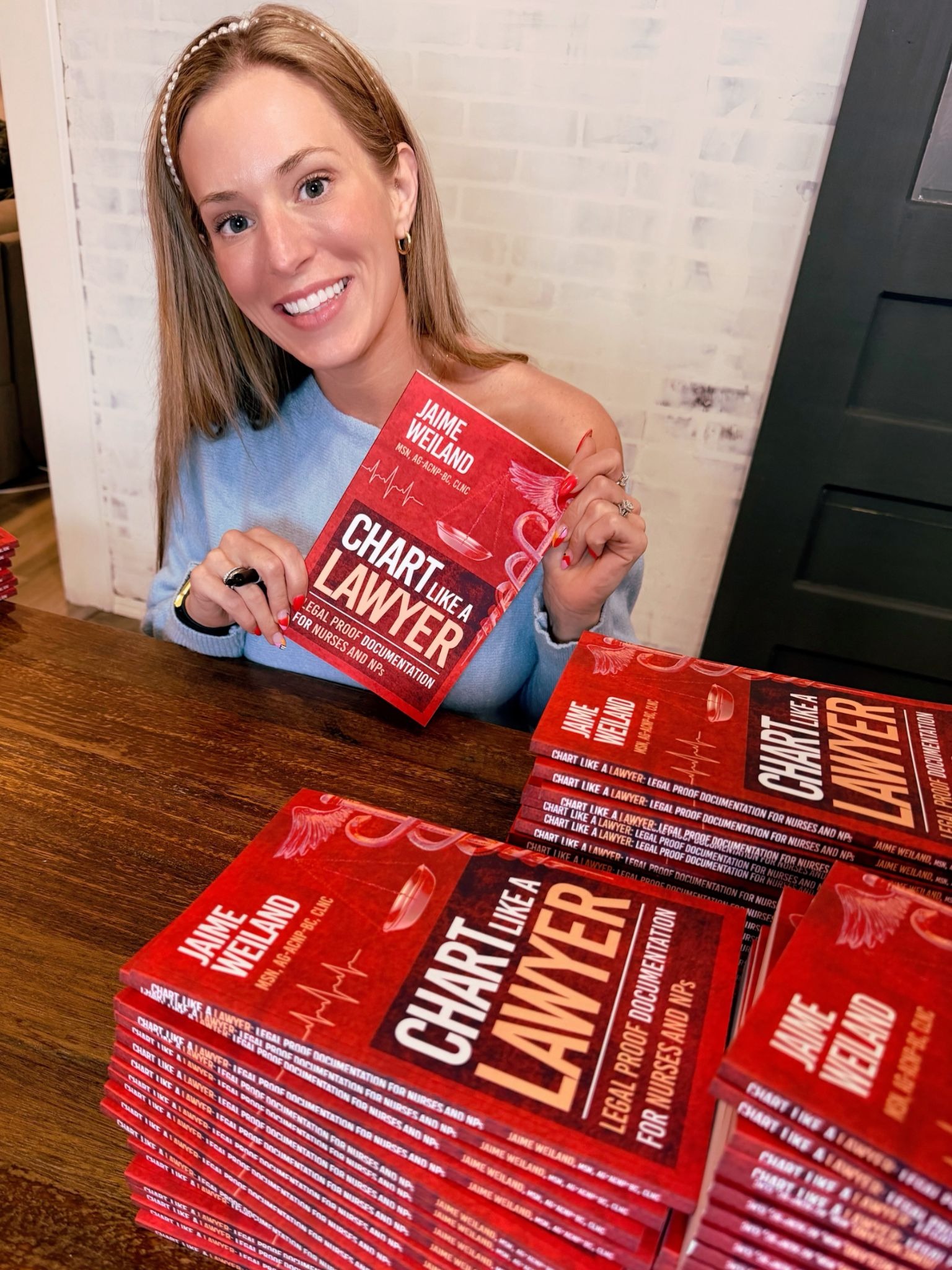 Jaime Weiland holding copies of “Chart Like a Lawyer” at a table stacked with books.