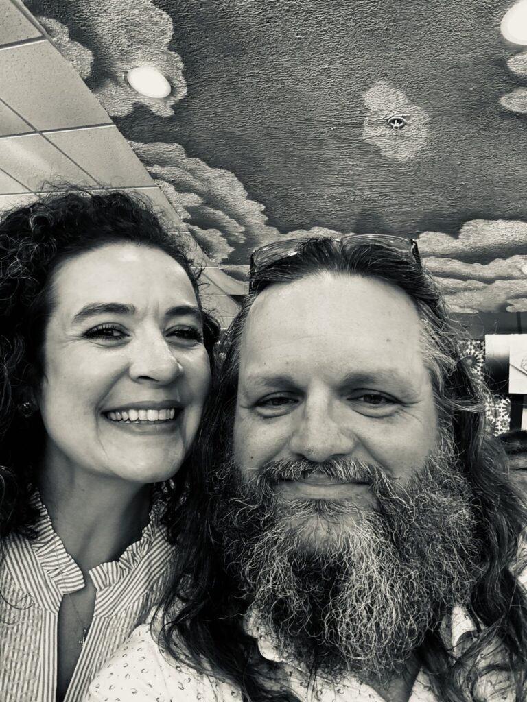 Justin Curatola smiling with a woman in a black-and-white selfie indoors.