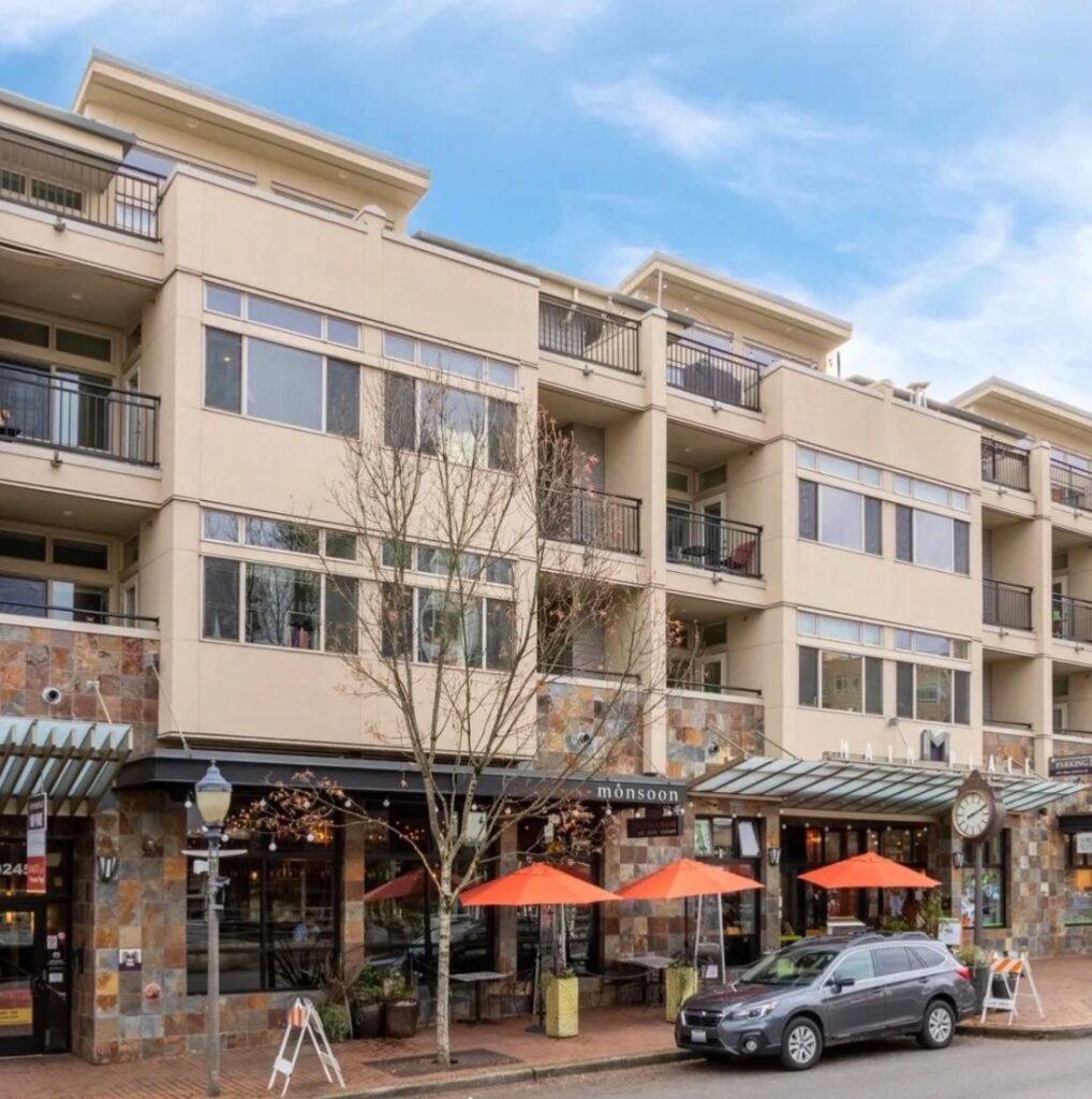 Mixed-use building with apartments, balconies, storefronts, outdoor seating, and a parked vehicle.