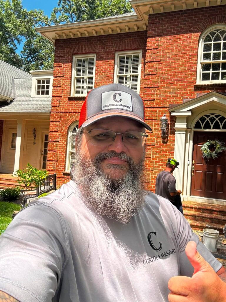Justin Curatola outside a historic brick home wearing Curatola Masonry apparel during a masonry restoration project.
