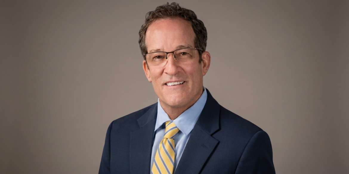 John Ziesing wearing a navy suit, blue shirt, and yellow striped tie.